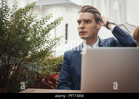 Junge attraktive Geschäftsmann neben Laptop und berühren die Haare sitzen. Stockfoto