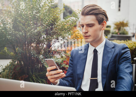 Junge Unternehmer mit Handy in der Hand und sitzt neben grüne Pflanze. Stockfoto