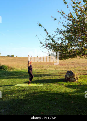 Von idyllischen ländlichen französischen Landschaft eine reife Frau übt ihre Yoga Positionen im schönen Herbst Sonne umgeben. Der Baum darstellen. Stockfoto
