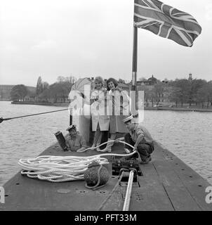 60er Jahre Mode. Zwei fashion Modelle und die Besatzung der Britischen u-boot Alcide. Das U-Boot liegt im Hafen von Stockholm verankert. Die Modelle tragen die herbste Mode Der regenjacken. Schweden Mai 1962 Stockfoto