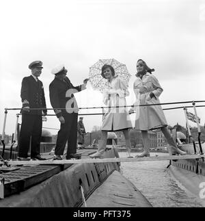 60er Jahre Mode. Zwei fashion Modelle und die Obersten der Britischen u-Boote Alcide und Orpheus. Die U-Boote im Hafen von Stockholm verankert. Die Modelle tragen die Herbste mode Mäntel und Schals. Schweden Mai 1962 Stockfoto