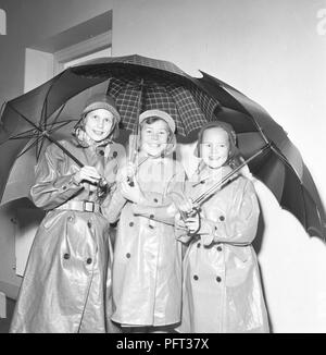 1950er Jahre Kinder in Regenkleidung. Drei Kinder stehen in togetherdressed Regenmäntel und Gummi mit Sonnenschirmen. Schweden November 1952 Stockfoto