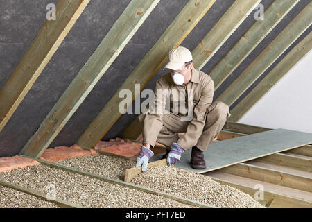 Mann, Overalls, Maske, Handschuhe und Mütze Nivellierung loose-fill-Isolierung zwischen den Deckenbalken Stockfoto