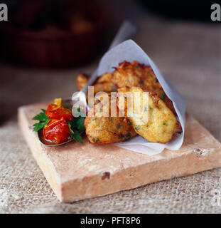 Croquetas de Bacalao (Stockfisch Kroketten) in einem Papier Kegel mit einem Löffel voll von Tomaten Salsa, auf eine Kachel, close-up Stockfoto