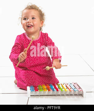 Kleines Mädchen (2 Jahre) kniend am Boden neben Xylophon Stockfoto