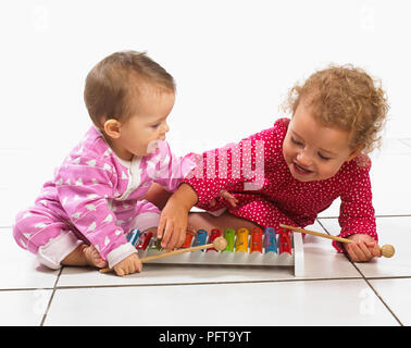 Kleines Mädchen (2 Jahre) und Baby (8 Monate) kniend auf dem Boden spielen ein Xylophon Stockfoto