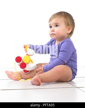 Baby Mädchen sitzen Spielen mit Ziehen entlang Spielzeug Ente, 12 Monate Stockfoto