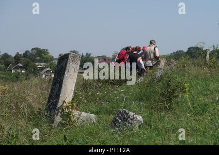 Die Teilnehmer der ROOTKA-Reiseagentur, die sich auf jüdische Kulturreisen in Osteuropa spezialisiert hat, stehen inmitten eines alten Grabsteines auf dem jüdischen Friedhof mit etwa 3000 Grabsteinen auf einem Hügel oberhalb des Flusses Zbruch, gegenüber der Stadt Sataniv im Rajon Horodok, Oblast Chmelnyzkyj, Ukraine. Im alten Teil befinden sich etwa 300 geschnitzte Grabsteine und Stelen aus dem 16.. Bis zur ersten Hälfte des 19.. Jahrhunderts. Der früheste Grabstein stammt aus dem Jahr 1554. Stockfoto