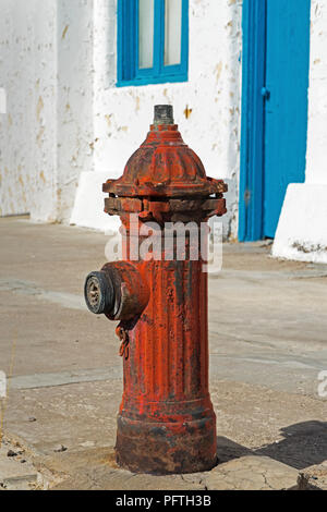 Eine helle rote Wasser Hydrant mit klöppel Ventil, alte weiß gestrichenen Gebäude mit abblätternder Farbe und helle blaue Tür und Fenster. Stockfoto