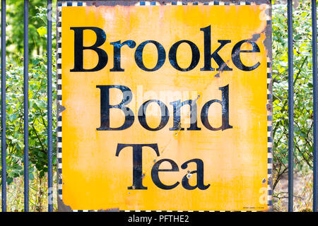 Nahaufnahme eines alten emaillierten Werbeschilders, Schilder an Geländern vor dem historischen Bahnhof „Brooke Bond Tea“ - britische Antiquitäten. Stockfoto