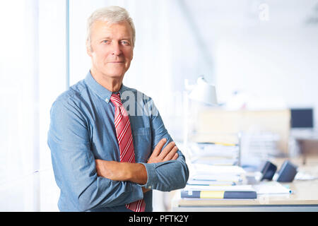 Porträt eines Executive senior Geschäftsmann an Büro mit verschränkten Armen. Stockfoto