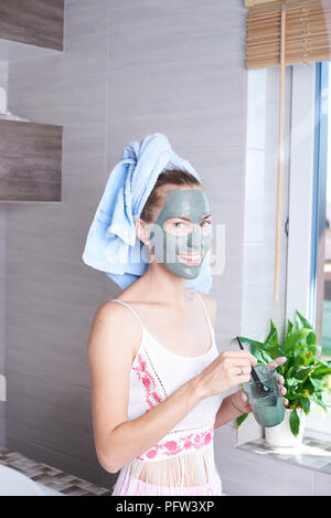 Frau Anwendung mask feuchtigkeitsspendende Creme im Gesicht in den Spiegel zu schauen. Mädchen kümmert um Ihrem Teint layering Feuchtigkeitscreme. Hautpflege spa Stockfoto