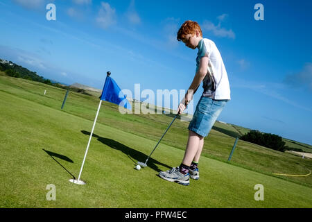 Junge Teenager üben, einen Golfball auf einem grünen. Cornwall Polzeath. Stockfoto