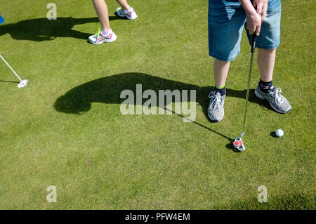 Beine von einem jungen Teenager Vorbereitung einer Golfkugel zu setzen. Cornwall Polzeath Stockfoto