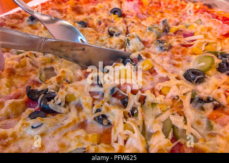 Eine Hand mit einem Messer und Gabel in Stücke schneidet Pizza Stockfoto