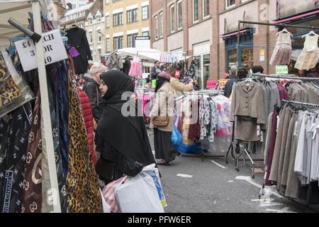 Kunden, einige tragende Hijab, Niqab, Spaziergang, und wechseln Sie in den Regalen von Kleidung auf der Straße an der Petticoat Lane Market, im East End, in London, England, 29. Oktober 2017. () Stockfoto