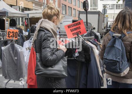 Zwei junge Frauen shop für Designer probe Mäntel, inmitten von Racks mit Kleidung auf der Straße an der Petticoat Lane Market, im East End, in London, England, 29. Oktober 2017. () Stockfoto