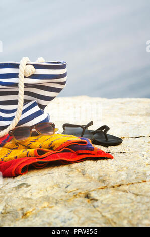 Sonnenbrille, Handtuch, Tasche und flip-flops am Strand. Sommerurlaub Konzept. Stockfoto
