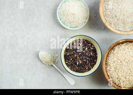 Verschiedene Arten von Reis in hölzernen Schüsseln wie Basmati, braun und schwarz auf grauem Hintergrund Stockfoto