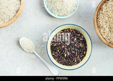 Verschiedene Arten von Reis in hölzernen Schüsseln wie Basmati, braun und schwarz auf grauem Hintergrund Stockfoto