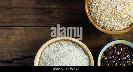Verschiedene Arten von Reis in hölzernen Schüsseln wie Basmati, braun und schwarz auf grauem Hintergrund Stockfoto