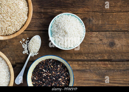 Verschiedene Arten von Reis in hölzernen Schüsseln wie Basmati, braun und schwarz auf grauem Hintergrund Stockfoto