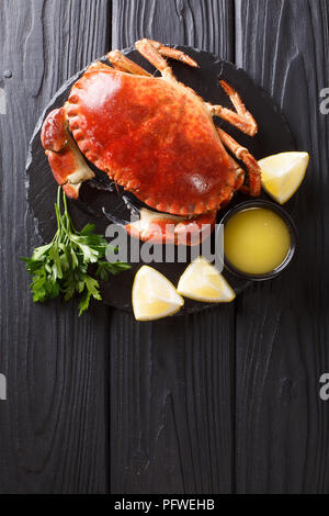 Serviert gekochten Leckerbissen brown Krabbe mit Soße, Zitrone und Petersilie auf einer Schiefertafel board Close-up auf einem schwarzen Holztisch. Leckeres Essen. Vertikale Ansicht von oben f Stockfoto