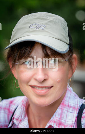 Nahaufnahme des trendigen 50-jährigen Weibchens in der Sportkappe, mit jungen Aussichten, locker gekleidet und auf eine Seite schauend, mit einem gruseligen Lächeln. Stockfoto