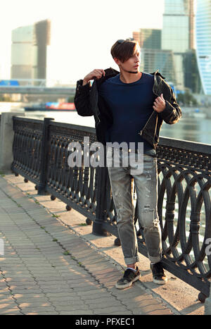 Denken gutaussehenden jungen Mann zu Fuß auf die Straße und Dressing fashion Jacke auf Stadtzentrum Hintergrund. Stockfoto