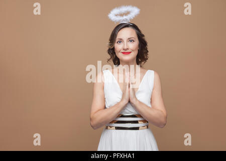 Elegant Angel brünette Frau in weißem Kleid und Nimbus im Kopf beten, und wenn man die Kamera mit einem Lächeln. Emotion und Gefühl Konzept. Studio s Stockfoto