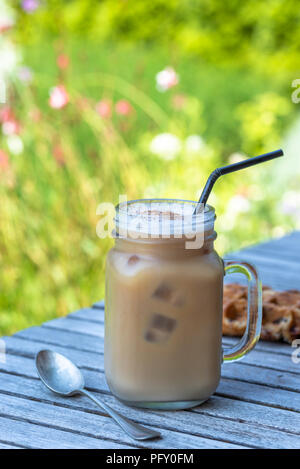 Eis Kaffee im Glas Becher mit Milch und Zimt auf hölzernen Tisch in den Garten. Stockfoto
