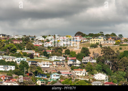 Burnie, Tasmanien, Australien - Dezember 15, 2009: Blick auf die Stadt zeigt, Sammlung von bunten Häusern auf grünem Hügel unter Dunkelgrau cloudscape eingestellt. Stockfoto