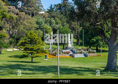 Burnie, Tasmanien, Australien - 15. Dezember 2009: Weiß Kriegerdenkmal Obelisk im Green Park mit gelben und roten Blüten der Innenstadt gesetzt. Stockfoto