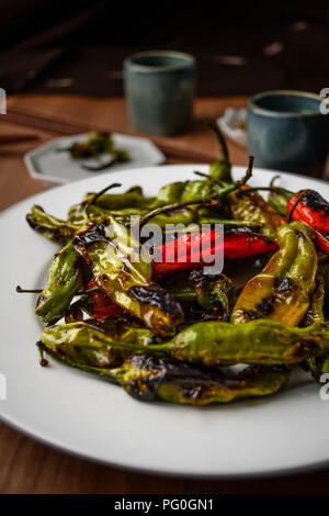 Verkohlte grüne und rote Paprika mit süßen togarashi shishito Spice auf einem runden weißen Teller serviert. Stockfoto