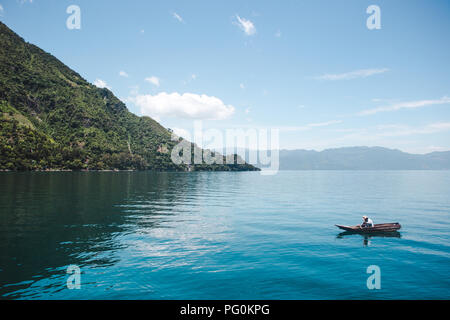 Einsame traditionelle Fischer sammelt seine Netze aus einem kleinen Kanu auf den Blauen, stillen Schönheit der Atitlán-See in Guatemala Stockfoto