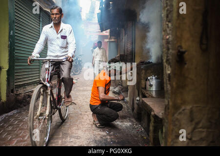 VARANASI, INDIEN - 20 Februar 2015: Street Hersteller macht Feuer für milchigen Kaffee in Kohle Ofen während der Radfahrer. Stockfoto