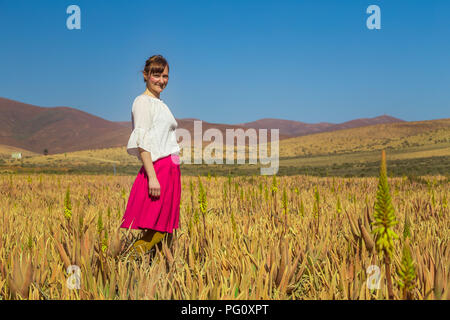 Junge Frau lächelnd und Blick in die Kamera in der Aloe vera Feld in Fuerteventura, Kanarische Inseln, Spanien. Stockfoto