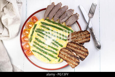 Omelett mit Spargel. Hausgemachten Schinken, Tomaten, Toast. Holz- hellen Hintergrund. Ansicht von oben Stockfoto