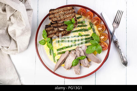 Omelett mit Spargel und Basilikum. Hausgemachten Schinken, Tomaten, Toast. Holz- hellen Hintergrund. Ansicht von oben Stockfoto