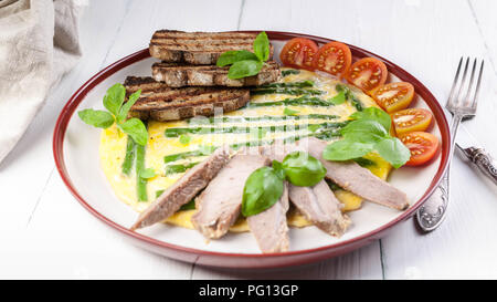 Omelett mit Spargel und Basilikum. Hausgemachten Schinken, Tomaten, Toast. Holz- hellen Hintergrund Stockfoto