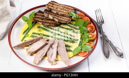 Frittata mit Spargel und Basilikum. Hausgemachten Schinken, Tomaten, Toast. Holz- hellen Hintergrund Stockfoto