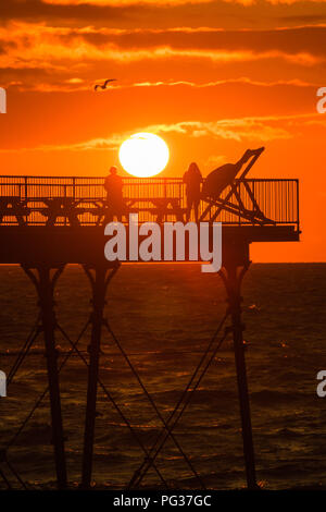 Aberystwyth Wales UK, Donnerstag, 23. August 2018 Großbritannien Wetter: eine atemberaubende Silhouette Sonnenuntergang über Menschen auf der Seebrücke in Aberystwyth stehend auf der Cardigan Bay Küste von West Wales, am Ende eines Tages des blustery kühle Winde und starke Regenschauer. Das Wetter für den August Bank Holiday Wochenende prognostiziert ist sehr mit schweren Regen wahrscheinlich für viele Bereiche Foto © Keith Morris/Alamy Leben Nachrichten unruhig zu werden. Stockfoto