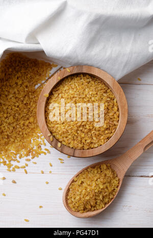 Ansicht von oben trocken Bulgur weizen in der Schüssel und Löffel auf Holz- Hintergrund. Stockfoto