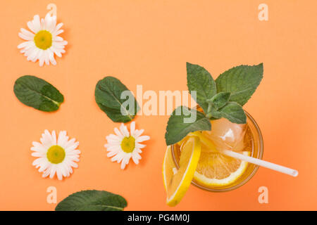 Hohes Glas kalter Sommer erfrischende Limonade mit Eis, Zitronenscheiben, Minze und Kamille Blumen auf Pfirsich farbigen Hintergrund. Ansicht von oben Stockfoto