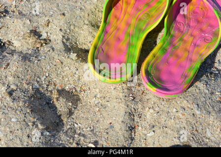 Pinkfarbene Damenpantoffeln mit grünen und gelben Scheidungen auf gelbem Sand mit flachem Muschelstrand am Schwarzen Meer am Nachmittag Stockfoto