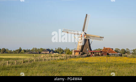 Holländische Windmühle aus Holz mit kleinen Miller Haus auf Landschaft bei Sonnenuntergang im Sommer mit Blumen Stockfoto