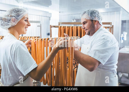 Frau arbeitet in der Metzgerei, Würstchen auf Strahl im Rack Stockfoto