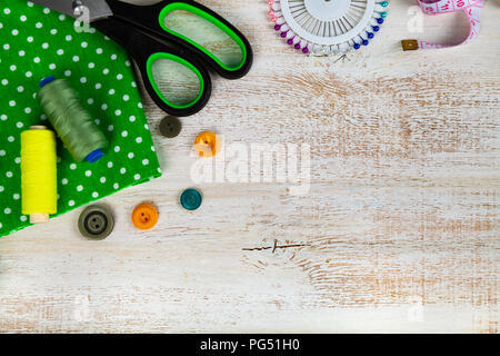 Nähzubehör und grünem Stoff auf einer hölzernen Hintergrund. Stoffen, Maßband, Pins, Buttons und Gewinde. Stockfoto