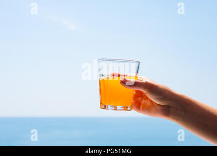 Ein Glas Saft in der Hand einer Frau. Ein Glas Saft vor dem Hintergrund des Meeres. Stockfoto