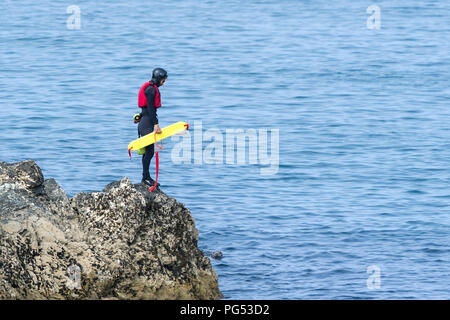 Ein coasteering Kursleiter steht auf einem Felsen und beobachtete ein grauer Dichtung auf der Landspitze in Newquay, Cornwall. Stockfoto